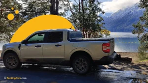 Camioneta plateada estacionada frente a un lago rodeado de montañas y árboles.