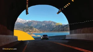 Auto saliendo de un túnel hacia lago y montañas nevadas en Mendoza.