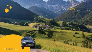 Auto en pradera verde con iglesia alpina y montañas Dolomitas al fondo.