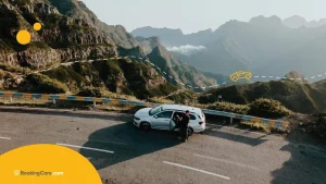Pareja junto a un auto blanco en una ruta de montaña con curvas pronunciadas.