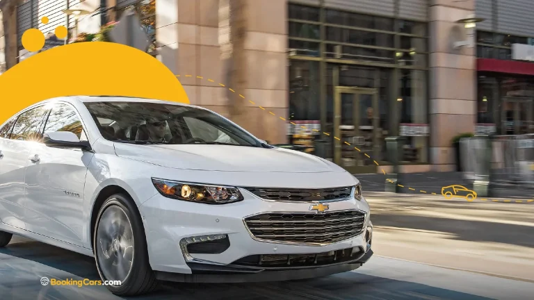 Sedán Chevrolet blanco conduciendo en calle urbana con gráfico amarillo superpuesto.