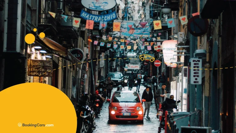 Calle estrecha en Roma con banderines, letreros y un Fiat rojo entre peatones.