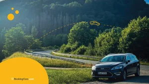 Auto en ruta de montaña rodeada de árboles bajo luz de atardecer.
