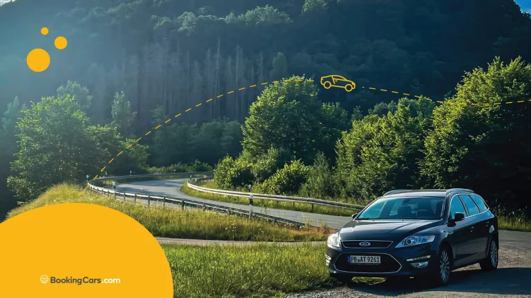 Auto en ruta de montaña rodeada de árboles bajo luz de atardecer.
