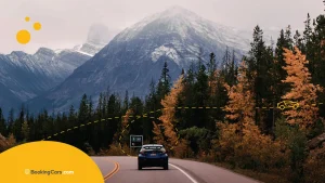 Auto en carretera canadiense rodeada de árboles otoñales y montañas nevadas.